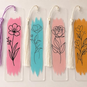 May include: Four rectangular clear acrylic bookmarks, each featuring a vertical brushstroke of color&mdash;pink, blue, light pink, and orange&mdash;with a black line-art floral illustration. Each bookmark includes a matching fabric tassel at the top.