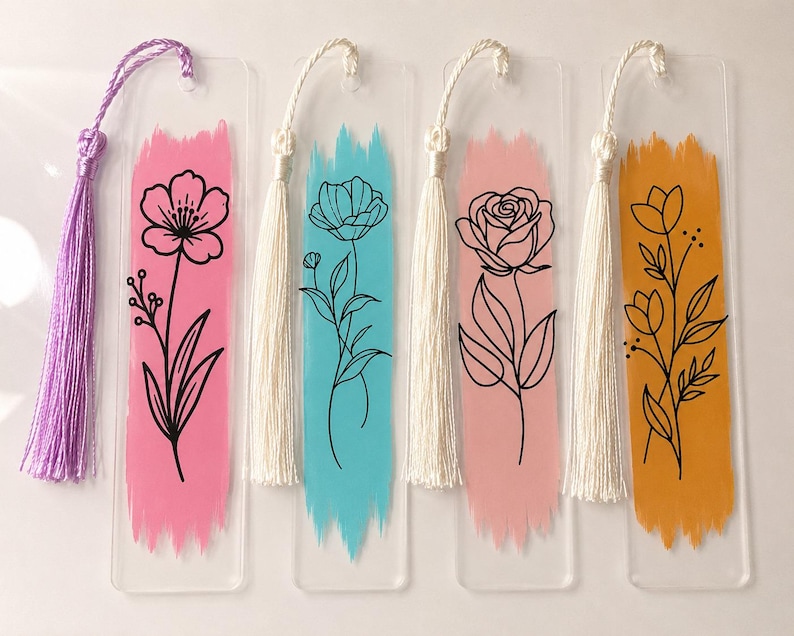 May include: Four rectangular clear acrylic bookmarks, each featuring a vertical brushstroke of color&mdash;pink, blue, light pink, and orange&mdash;with a black line-art floral illustration. Each bookmark includes a matching fabric tassel at the top.