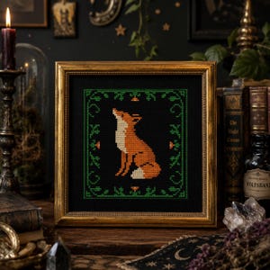 May include: A framed cross-stitch depicting an orange fox with a white underbelly on a black backdrop. The fox is surrounded by a green border with floral details. The frame is gold-coloured, creating a rustic and decorative piece for the home.