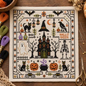 Op de afbeelding: Een vierkant kruissteekpatroon op crèmekleurige stof met Halloween-motieven, waaronder een centraal spookhuis, een geest, een skelet, zwarte katten, pompoenen, vleermuizen, een heksenhoed en een ketel, met de tekst "BOO" en "HALLOWEEN" geborduurd in zwart en oranje.