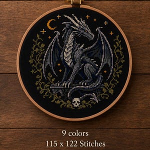 May include: A cross-stitch embroidery of a dragon in a wooden hoop. The dragon is gray and black, with a white chest, and is set against a black background with a crescent moon and stars. The text reads "9 colors, 115 x 122 Stitches (8.2 x 8.7 in.)".
