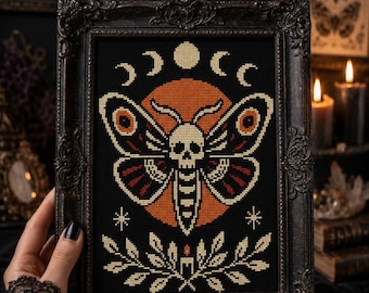 May include: A framed cross-stitch featuring a moth with a skull design, set against a black background with an orange moon. The moth has red and cream details. The frame is ornate and dark. The image also includes the text "STAY WILD MOON CHILD".