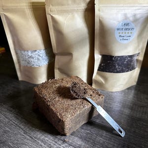 Pode incluir: Três sacos de papel castanho com conteúdo visível, incluindo um pó claro e grânulos escuros. Um bloco retangular castanho de material comprimido está na frente, com uma pequena colher de medição de metal em cima. O texto "Love your order? Please Leave a Review!" está num autocolante.