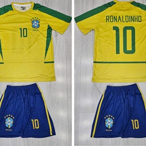 May include: A yellow and green Brazil soccer jersey and shorts set. The jersey has the number 10 on the front and back, with the name RONALDINHO on the back. The shorts are blue with the number 10.