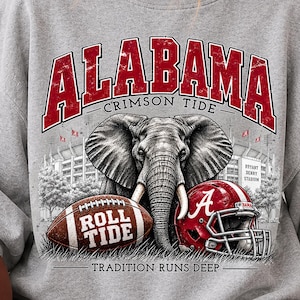 May include: A heather gray crewneck sweatshirt featuring a graphic print with the text ALABAMA CRIMSON TIDE, ROLL TIDE, and TRADITION RUNS DEEP. The design includes an elephant, a football, and a red football helmet with a white A logo.