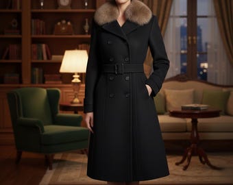 May include: A black double-breasted coat with a belted waist and a fur collar. The coat has a knee-length hemline and is worn by a person. The background includes a green armchair, a lamp, and a sofa.