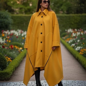 May include: A mustard yellow coat with black trim and buttons. The coat has a unique, asymmetrical design and is worn with black boots. The background features a garden with a stone path and colorful flowers.