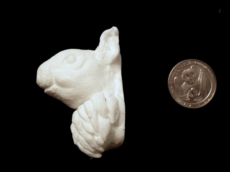 K&ouml;nnte beinhalten: Wei&szlig;e Keramikskulptur eines Eichh&ouml;rnchenkopfes und Vorderpfoten, das Eichh&ouml;rnchen schaut nach rechts. Die Skulptur ist etwa so gro&szlig; wie eine deutsche 2-Euro-M&uuml;nze.