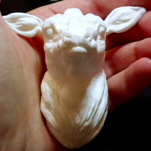 Op de afbeelding: Witte keramische sculptuur van een hertenkop met gedetailleerde vachtstructuur. Het beeldje wordt in de hand van een persoon gehouden.