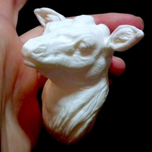 Op de afbeelding: Witte keramische sculptuur van een hertenkop met gedetailleerde kenmerken. Het beeldje wordt in de hand van een persoon gehouden.
