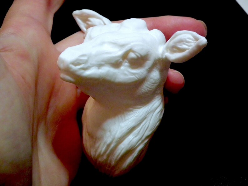 Op de afbeelding: Witte keramische sculptuur van een hertenkop met gedetailleerde kenmerken. Het beeldje wordt in de hand van een persoon gehouden.