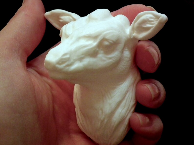 Op de afbeelding: Witte keramische sculptuur van een hertenkop met gedetailleerde kenmerken. Het beeldje wordt in een hand gehouden.
