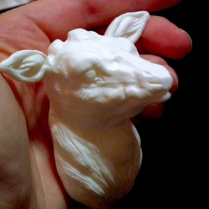 Op de afbeelding: Witte keramische sculptuur van een hertenkop met gedetailleerde kenmerken. Het beeldje wordt in een hand gehouden.