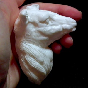 Op de afbeelding: Witte keramische sculptuur van een dierenkop, mogelijk een wolf of een hond, met gedetailleerde vachttextuur. De sculptuur wordt in een hand gehouden.