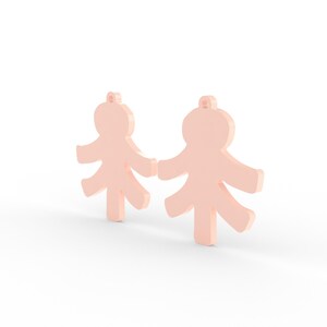 May include: Two light peach-colored, stylized human figure pendants. Each pendant has a loop at the top for hanging and outstretched arms and legs. The figures are standing upright, with a simple, minimalist design.