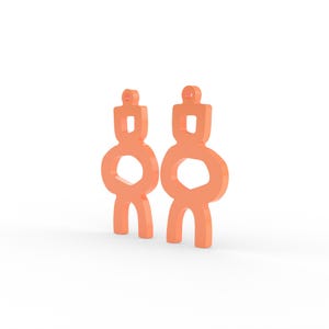 May include: Two peach-colored abstract earrings. Each earring has a rectangular top, a circular middle, and two curved legs. The earrings are displayed against a white background.