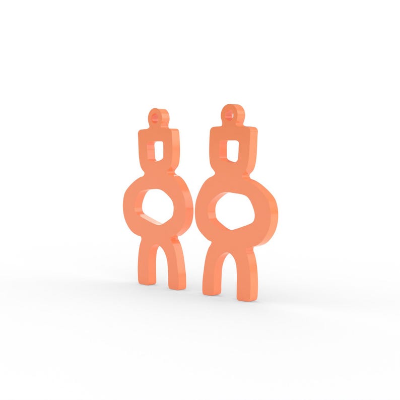 May include: Two peach-colored abstract earrings. Each earring has a rectangular top, a circular middle, and two curved legs. The earrings are displayed against a white background.