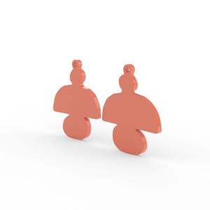 May include: Two coral-colored earrings with a unique, abstract design. Each earring features a rounded top, a flared middle section, and a circular bottom. The earrings are displayed against a white background.