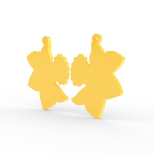 K&ouml;nnte beinhalten: Zwei gelbe ohrringf&ouml;rmige Narzissen. Jeder Ohrring hat eine Schlaufe zum Aufh&auml;ngen und eine detaillierte Mitte. Die Ohrringe sind leuchtend gelb und vor einem wei&szlig;en Hintergrund platziert.