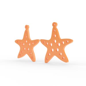 Puede incluir: Dos dijes con forma de estrella de mar de color naranja con un acabado liso y m&uacute;ltiples recortes circulares en todo el cuerpo. Cada dije presenta un peque&ntilde;o lazo en la punta superior, dise&ntilde;ado para sujetarse a joyas u otros objetos.