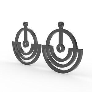 May include: A pair of dark gray earrings with a geometric design. Each earring features a circular top with a vertical bar and a small circle, connected to a semi-circular base with two curved lines. The earrings are displayed against a white background.