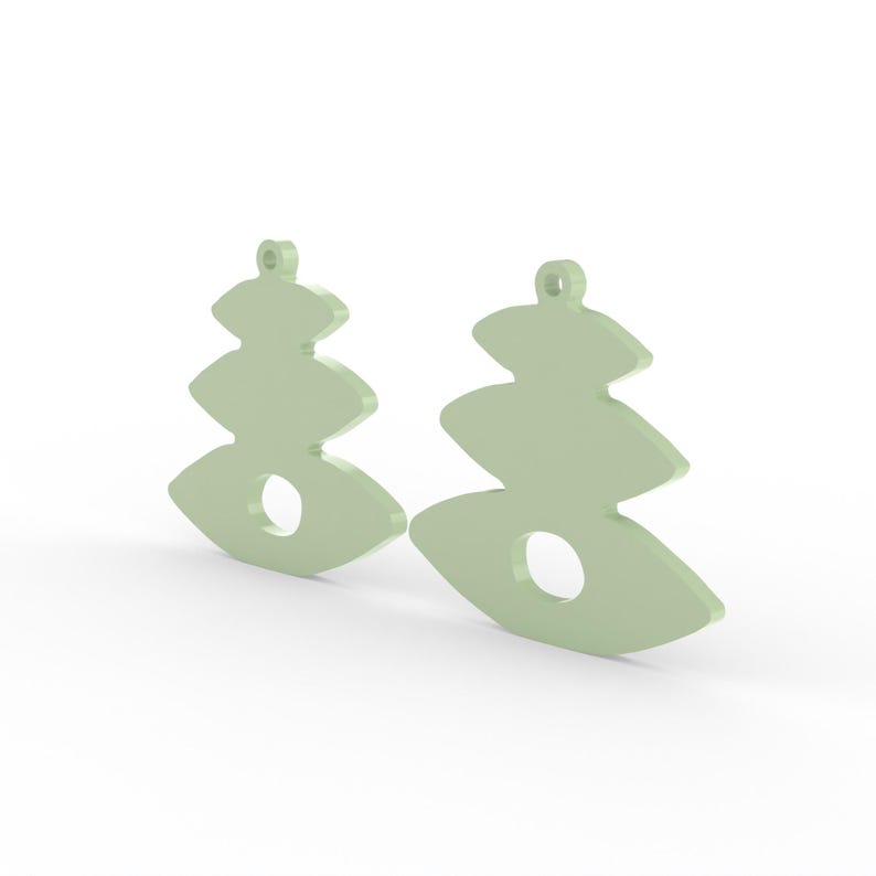 May include: Two light green, abstract-shaped earrings. Each earring has a layered design with a circular cutout in the center. The earrings have a small loop at the top for hanging.
