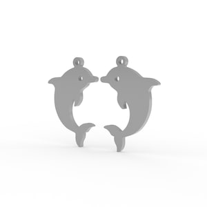Puede incluir: Dos dijes de delf&iacute;n de metal en tono plateado, cada uno con una superficie lisa y plana y un peque&ntilde;o lazo circular en la parte superior para su fijaci&oacute;n. Los delfines est&aacute;n orientados uno frente al otro, mostrando un dise&ntilde;o de silueta simple.