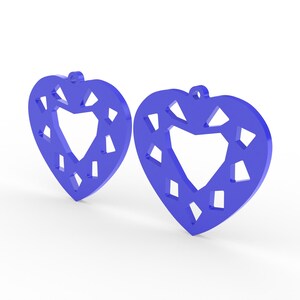 May include: Two blue heart-shaped earrings with a geometric design. Each earring features a heart-shaped cutout in the center and smaller diamond-shaped cutouts around the edges. The earrings have a small loop at the top for hanging.