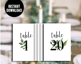 May include: Two white table number cards with green foliage and black calligraphy. The first card says "table 1" and the second card says "table 20".