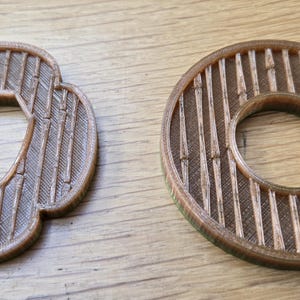 May include: Two 3D-printed tsuba sword guards in a metallic bronze finish. One guard features a four-lobed mokko shape with a central hexagonal opening, while the other is circular with a round centre hole. Both display a vertical bamboo pattern.