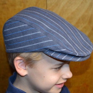 Pode incluir: Um boné de newsboy listrado azul e branco com topo plano e aba curva.