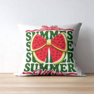 Op de afbeelding: Wit vierkant kussen met een watermeloen strik ontwerp. De strik is gemaakt van rode watermeloen schijfjes met zwarte pitjes en een groene schil. Het kussen heeft de woorden "SUMMER" en "Summer Vibes" in groen en rood.