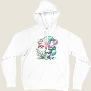 May include: White hooded sweatshirt featuring a whimsical gnome illustration. The gnome is depicted in pastel colors, wearing a hat and holding a gift bag. The design includes floral and snowflake accents, creating a festive and charming aesthetic.