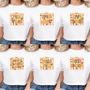 K&ouml;nnte beinhalten: Ein wei&szlig;es T-Shirt mit einer quadratischen Grafik mit gewelltem Rand. Die Grafik enth&auml;lt herbstliche Schriftz&uuml;ge und Illustrationen wie K&uuml;rbisse, Bl&auml;tter und Eicheln in Orange, Gelb, Gr&uuml;n und Braun. Der Text lautet Fall Vibes, Spice Girl, Give Thanks, Grateful Thankful Blessed, Hello Fall oder Cozy Season.