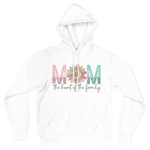 May include: White hoodie with the word "MOM" in pink, teal, and floral-patterned letters, with a sunflower in the center. Below the word "MOM" is the phrase "the heart of the family" in a black script font.