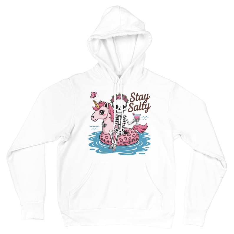 Op de afbeelding: Witte hoodie met een afbeelding van een skelet dat ontspant op een roze eenhoorn drijver in het water. Het skelet houdt een drankje vast en de tekst "Stay Salty" staat erboven. Er is ook een roze vlinder aanwezig.