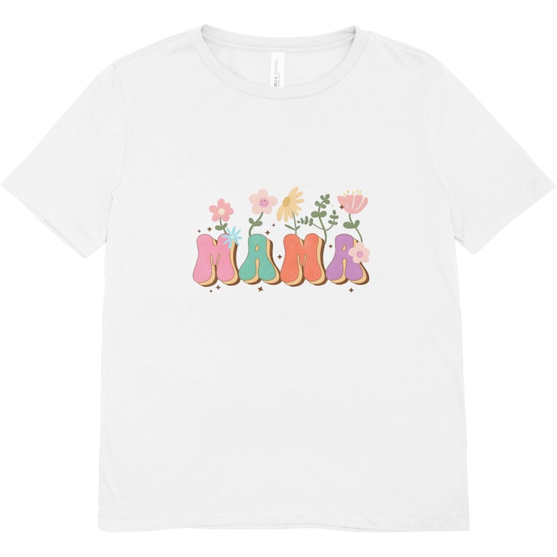 May include: White t-shirt featuring the word "MAMA" in colorful, retro bubble letters, with flowers sprouting from the letters. The design includes pink, teal, orange, and purple hues, with a brown outline.