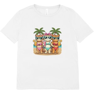 Op de afbeelding: Wit t-shirt met een afbeelding van drie cartoonkatten op een strand. De katten dragen zonnebrillen en bikini's en houden drankjes vast. Palmbomen staan op de achtergrond. Het ontwerp is gedrukt op een wit t-shirt met korte mouwen.
