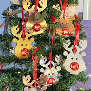 Puede incluir: Un árbol de Navidad decorado con adornos de renos. Los adornos son dorados y plateados con cintas rojas. Cada reno tiene una bola roja y dorada. El árbol es verde con luces.