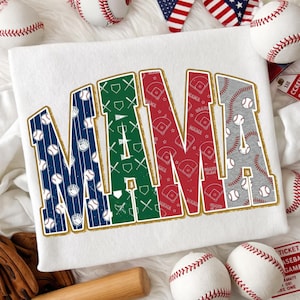 May include: White sweatshirt with the word "MAMA" in large, colorful letters. The letters are filled with baseball-themed patterns and outlined in gold. Baseball and related items are scattered around the sweatshirt.