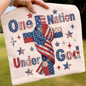 Puede incluir: Una bolsa con cremallera de color crema con imágenes patrióticas. El diseño incluye las palabras "One Nation Under God" en rojo y azul, junto con estrellas y una bandera estadounidense estilizada.