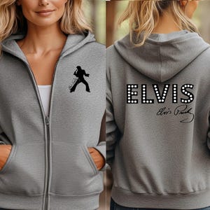 Pu&ograve; includere: Una felpa con cappuccio e zip grigio melange con la silhouette nera di un cantante sul petto sinistro. Il retro mostra la scritta ELVIS in un carattere a pois bianchi con una firma nera sottostante. Il capo &egrave; dotato di cappuccio e due tasche.