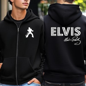 May include: A black zip-up hoodie featuring a white silhouette of Elvis Presley on the left chest. The back displays the word ELVIS in a large, dotted white font, accompanied by the signature of Elvis Presley printed in white below the text.