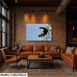 May include: A framed canvas print depicting a bald eagle in flight against a blue sky. The eagle is perched on a tree branch with white flowers. The print is 102x152cm and hangs above a brown leather sofa.