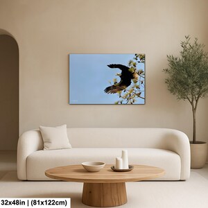 May include: A canvas print depicting a bald eagle in flight against a blue sky. The eagle, with dark brown wings and a white head, is captured mid-flight near a tree. The print is 81x122cm.