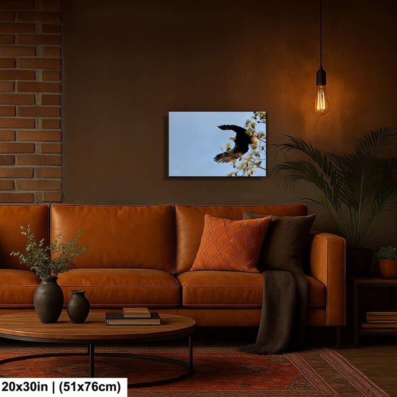 May include: A framed canvas print showing a bird in flight against a light blue sky, with white blossoms. The artwork is 20x30 inches (51x76cm). The print is displayed above a brown leather sofa.