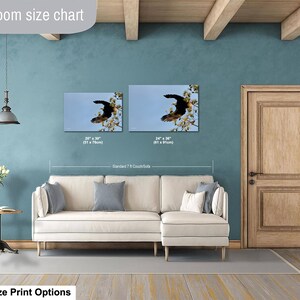 May include: Two framed canvas prints of a soaring eagle against a blue sky, displayed above a cream-coloured sectional sofa. The prints are 51 x 76cm and 61 x 91cm. The room has a teal wall and a wooden door.