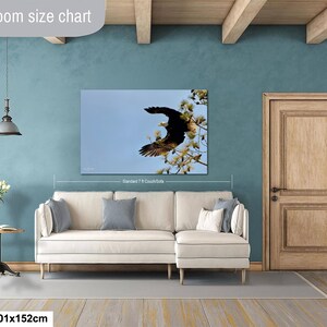 May include: A framed canvas print of a bald eagle in flight, set against a blue sky and tree branches. The artwork is displayed above a cream-colored sectional sofa. The dimensions are 101x152cm.