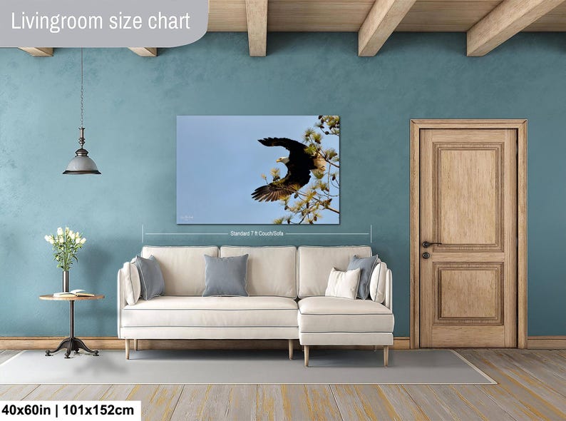 May include: A framed canvas print of a bald eagle in flight, set against a blue sky and tree branches. The artwork is displayed above a cream-colored sectional sofa. The dimensions are 101x152cm.