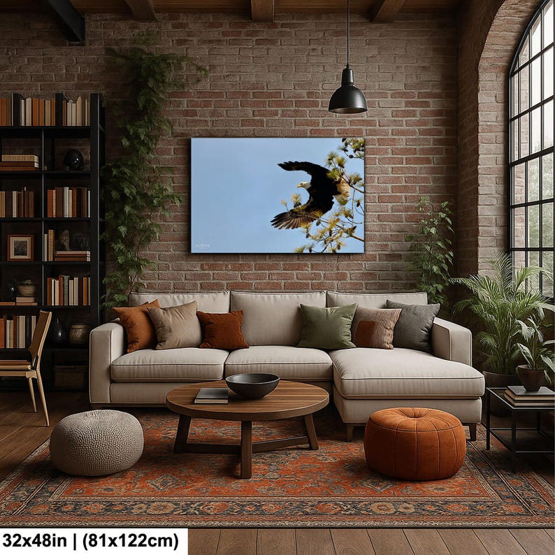 May include: A framed canvas print of an eagle in flight against a blue sky hangs above a beige sectional sofa. The living room features a brick wall, a wooden coffee table, and a patterned rug. The print measures 81x122cm.